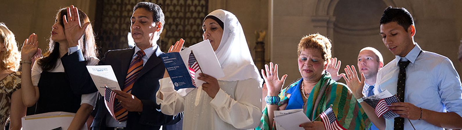 Naturalization Ceremony with new citizens holding hands up as they swear their oath