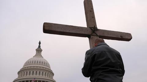 A man is holding a large wooden cross in front of the US capitol building, photo credit Win McNamee, Getty Images