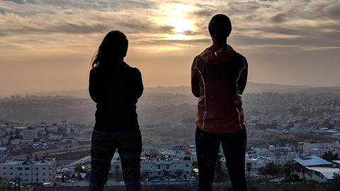 Two students looking out at a city landscape, silhouetted by the sunset