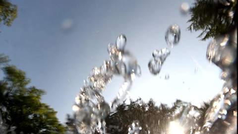 Film still by Sharon Harper, a blue sky and trees with waterdrops in the foreground on the lens