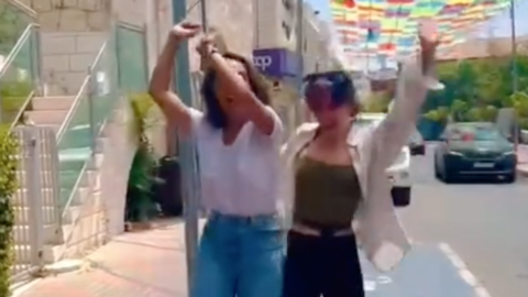 Sami and Ciara hipbump on a street with colorful umbrellas hanging overhead