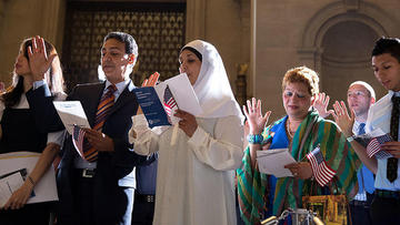Naturalization Ceremony with new citizens holding hands up as they swear their oath