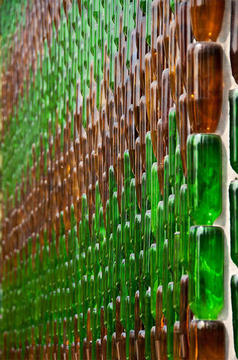 Rows of green and brown beer bottles create an attractive pattern on a white wall.