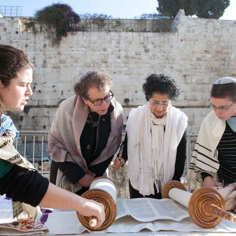 Four women wearing tallit read from a Torah scroll