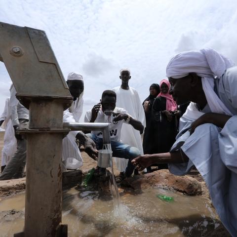Adults and young people collect and drink cups of water from a well in the middle of the desert.