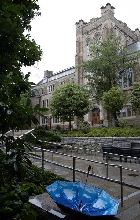 A black upside-down umbrella shows its inside pattern of a blue sky. It sits in front of Swartz Hall on a rainy day.