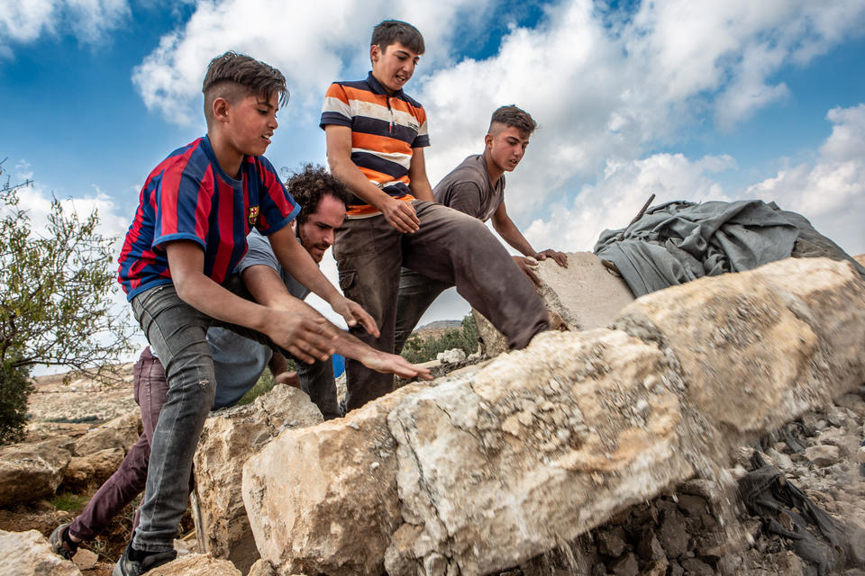 A man with three young boys are perched on a large rock